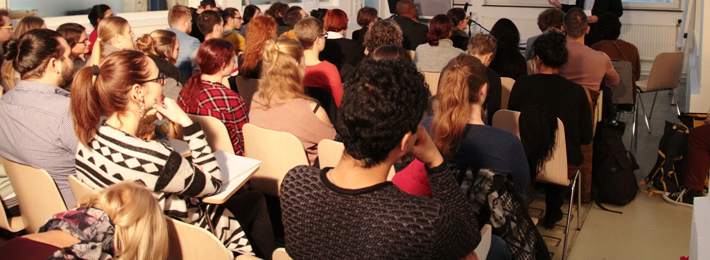 Ein großer Raum mit Sesselreihen und vielen Menschen bei einem Vortrag