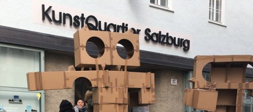Das Bild zeigt die Köpfe zweier Kartonfiguren vor dem Eingang des Kunstquartier salzburg