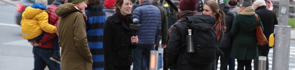 eine Person wird von zwei jungen Frauen mit Mikro und Kamera interviewt
